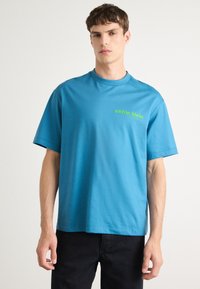 Μπλε κοντομάνικο μπλουζάκι από βαμβάκι, με χαλαρή εφαρμογή. Σημαντικό πράσινο λογότυπο "Calvin Klein" στο στήθος. Απαλή υφή.