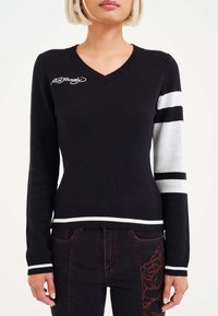 Black knit sweater with a v-neck, white stripes on one sleeve, and a logo on the chest; ribbed cuffs and hem detail.