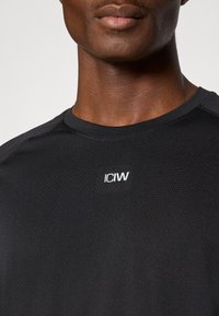 Μαύρο αθλητικό μπλουζάκι με στρογγυλή λαιμόκοψη, κατασκευασμένο από λείο, ελαστικό ύφασμα· διαθέτει λευκό λογότυπο "ICIW" στο στήθος.
