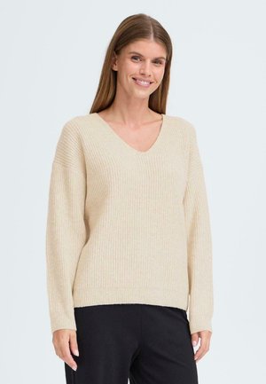 Beige ribbad stickad tröja med V-hals, lös passform och långa ärmar. Texturerad tyg och kontrasterande nederkantdetalj.