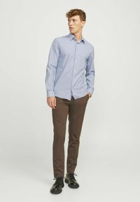 Camicia azzurra a maniche lunghe con colletto classico e bottoni; abbinata a pantaloni slim-fit marroni e scarpe nere. Colori solidi, texture morbida.