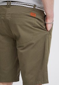 Olivgrüne Shorts mit regulärer Passform, ausgestattet mit Gesäßtaschen, einem gestickten Design und einem markierten Lederpatch am Bund.