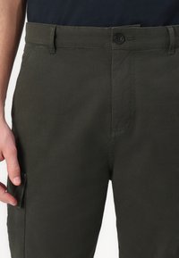 Pantalons légers de couleur vert foncé avec une texture lisse, dotés d'une fermeture à bouton, de passants de ceinture et d'une poche latérale pour le rangement.