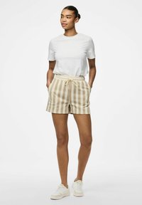 T-shirt blanche à manches courtes associée à un short beige rayé avec une taille élastique et un cordon de serrage. Baskets de couleur claire.