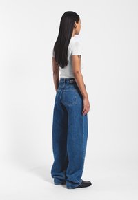 Jeans de mezclilla azul de talle alto con un ajuste holgado, que cuentan con un diseño clásico de cinco bolsillos y una etiqueta de marca visible en la cinturilla.
