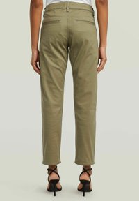 Pantalons droit en mélange de coton vert olive, avec deux poches arrière et ourlets roulés, assortis à des sandales à talons hauts noires à lanières.