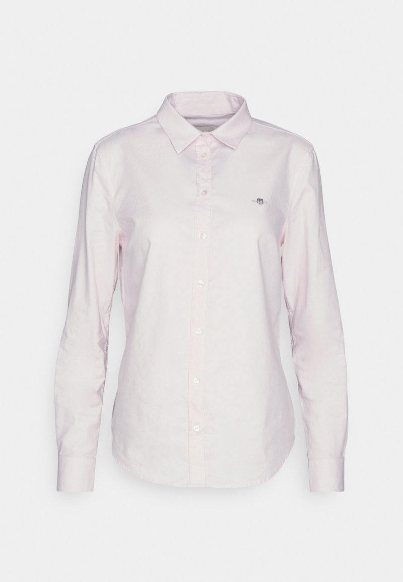 Chemise rose clair à manches longues avec un col classique, comportant des boutons blancs et un petit logo brodé sur la poitrine.