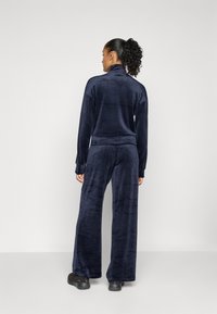 Ein marineblauer Velours-Trainingsanzug mit hohem Kragen, langen Ärmeln und weit geschnittenen Hosen aus einem weichen Material und lockerer Passform.