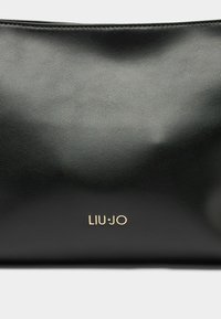 Sort lædertaske med en glat overflade, der har et synligt guldlogo nederst. Kompakt design med diskrete syninger.