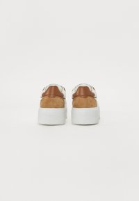 Sneakers med hvitt skinn og brune semskede accenter, med en kraftig hvit såle og en teksturert hælflik, merket "LOVE MOSCHINO."