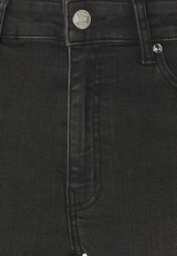 Gros plan sur le devant d'un jean en denim noir avec braguette zippée, bouton argenté et coutures visibles.