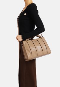 Borsa a tracolla in pelle beige con design plissettato, manici intrecciati e superficie liscia. Presenta un dettaglio del logo sul davanti e una forma strutturata.