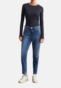Maglietta a maniche lunghe nera a costine abbinata a jeans blu a vita alta, con cinque tasche, orli strappati e sneakers bianche.
