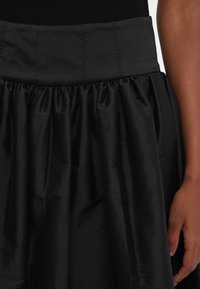 Fustă neagră cu talie structurată și material plisat. Textură asemănătoare satinului, cu o finisare netedă și un luciu subtil.