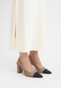 Bežid slingback kontsad, millel on terav must varbakate ja paks konts. Sile nahkviimistlus õrna sära ja minimalistlikud disainielemendid.