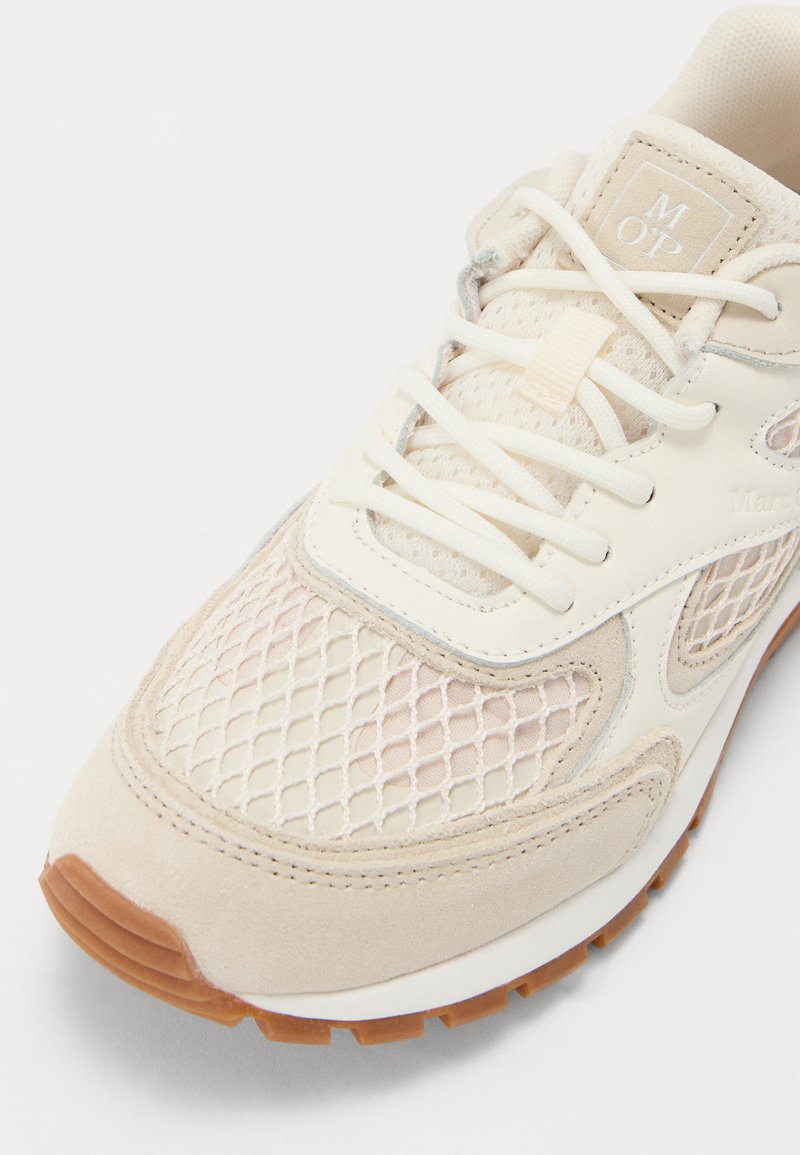 Beige Sportlichkeitsschuh mit Mesh-Obermaterial, Wildlederelementen und weißer Gummisohle. Mit flachen Schnürsenkeln und Logo auf der Zunge.
