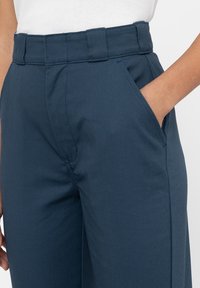 Marinblå byxor med hög midja, utrustade med sidfickor och ett mjukt, strukturerat tyg. Skräddarsydd passform med synliga sömmar.