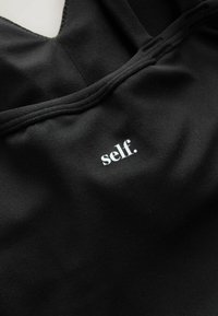 Top sportivo nero con scollo a barca, realizzato in morbido tessuto, con un piccolo logo stampato bianco che recita "self." vicino al centro.