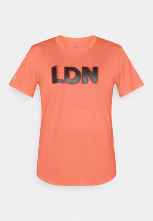 T-shirt de sport à manches courtes, couleur corail, avec un tissu en maille texturée et un grand imprimé noir "LDN" sur le devant.