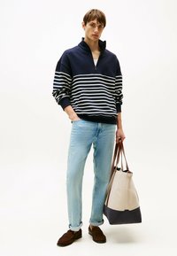 Pullover a righe navy e bianche con zip a quarti, jeans dritti blu chiaro, mocassini marroni e una borsa tote beige e navy.