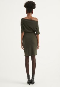 Olivgrünes, schulterfreies Kleid mit kurzen Ärmeln, taillierter Form, gerippter Textur und mittlerer Oberschenkellänge, kombiniert mit schwarzen Stiefeletten.