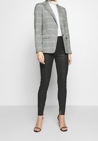 Grijs geruite blazer met schmallen revers, twee voorzakken, gecombineerd met strakke zwarte broek met zijsplitsen. Model draagt zwart met leren hakken.