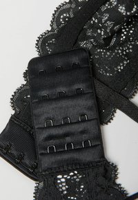 Černý krajkový oděv s propracovanými květinovými vzory, s texturovaným páskem a několika háčky a očky pro nastavitelné uchycení.
