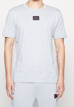 Homme portant un ensemble T-shirt à manches courtes et shorts gris clair, tous deux avec des patchs noirs portant l'inscription « HUGO » en lettres rouges.