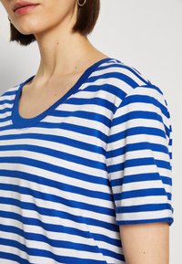 Camiseta de rayas azul y blanca con escote redondeado y mangas cortas. Hecha de una tela suave, presenta un ajuste casual y una textura lisa.