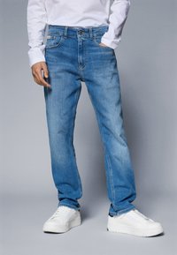 Lys blå denimjeans med rett snitt, fem lommer, knappelukking og subtil falming. Kombinert med hvite sportsko.