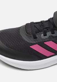 Zapatilla deportiva negra con acentos rosas, parte superior de textil, suela de goma y diseño con cordones que presenta tres franjas rosas en el lateral.