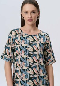 Bluse mit Blumenmuster und kurzen Ärmeln, die lebendige Blätter in Grün, Blau und Pfirsich auf einem dunklen Hintergrund zeigt. Glatte Stofftextur.