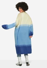 Cardigan lavorato a maglia lunghezza ginocchio con sfumatura dal crema al blu, con un motivo di piccoli disegni vicino all'orlo e maniche larghe.
