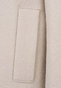 Hellbeige Wollmantel mit einer strukturierten Oberfläche und einer einzelnen gesteppte Tasche auf der Vorderseite. Einfaches, schlankes Design ohne Verzierungen.