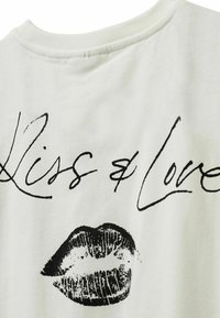 Valkoinen puuvillapaita, jossa on musta teksti "Kiss & Love" ja printattu huuligrafiikka. Pehmeä kangas, pyöreä kaula-aukko, rento muotoilu.
