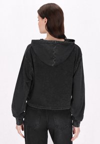 Fekete farmer kapucnis pulóver, rövid fazonban, puha tapintással, hosszú ujjakkal és rögzített kapucnival. Minimalista design, látható logók vagy minták nélkül.