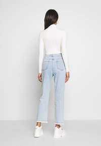 Haut à col roulé blanc ajusté en maille côtelée, associé à un jean bleu clair taille haute à coupe décontractée et ourlets effilochés, porté avec des baskets blanches.