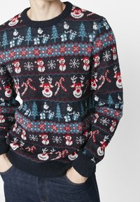 Marinblå stickad tröja med julmotiv: snögubbar, renar, träd och snöflingor i röd och blå. Ribbad halsringning och ärmslut.