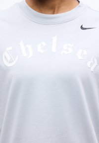 Λευκό φούτερ με τη λέξη «Chelsea» σε λευκά γοτθικά γράμματα και ένα μικρό μαύρο λογότυπο Nike στο επάνω δεξί μέρος του στήθους.