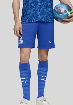 Blauwe voetbalkorte broek en sokken van ademend materiaal. De shorts hebben een wit logo. De sokken hebben een gestreept patroon met een logo en tekst.