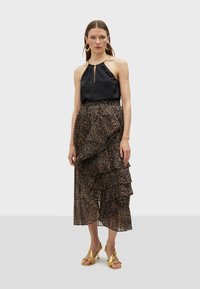 Black satin halter top with a keyhole detail paired with a tiered, pleated skirt featuring a leopard print in shades of brown and black. Gold sandals.