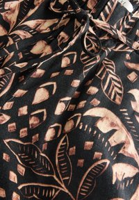 Tissu noir avec des motifs beiges de feuilles, de losanges et de soleil abstrait, et un cordon noué à la taille.