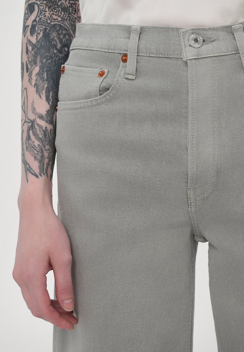 Gray denim jeans with a high waist, featuring orange accents on the pockets, a silver button closure, and a smooth, textured finish.