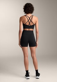 Top sportiv negru, scurt, cu bretele încrucișate, purtat cu pantaloni scurți negri ajustați. Țesătură netedă, design minimal și talie înaltă.
