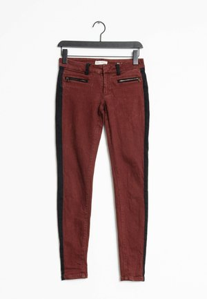 Pantalons en denim rouge avec des panneaux latéraux noirs, dotés de poches avant zippées et d'une coupe slim. Fabriqués en tissu doux, avec une texture minimale.