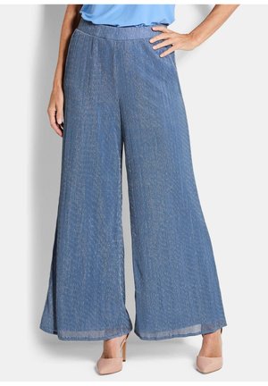 Frau trägt hochgeschnittene, weit geschnittene blaue Hose mit dezenten vertikalen Streifen und hautfarbene High Heels, steht mit einer Hand in der Hüfte.