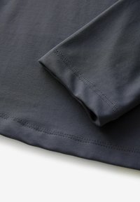Donkergrijze stof met een gladde textuur, voorzien van een casual hemlijn en manchet, waarmee nette stiksels langs de randen worden getoond.