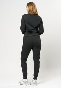Svart sweatshirt och matchande joggers i mjukt material. Har en figurnära design med ribbade muddarna och midjan, kombinerat med vita sneakers.