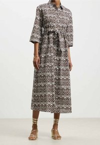 Brun och vit mönstrad skjortklänning med trekvartslånga ärmar, bälte i midjan och en flödande kjol, tillverkad av ett lätt tyg.