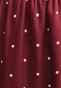 Burgunderfarbener Stoff mit weißen Polka Dots, mit texturierter Oberfläche und gerafftem Bund, der ein weiches, fließendes Erscheinungsbild bietet.